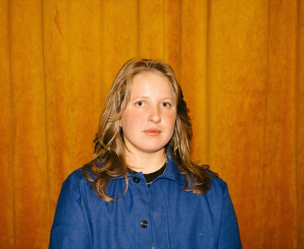Caitlin Reilly in a blue jacket in front of an orange curtain